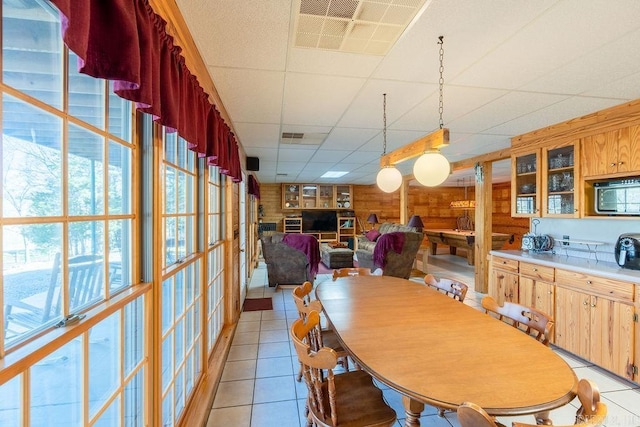 tiled dining room featuring wood walls and a drop ceiling