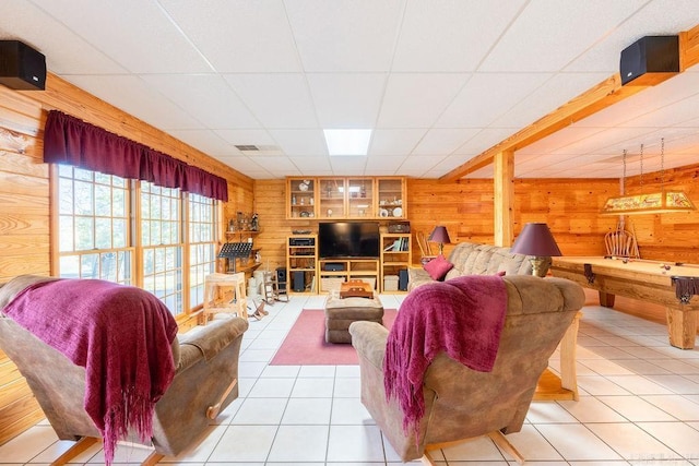 living room with light tile patterned floors, a drop ceiling, and wooden walls