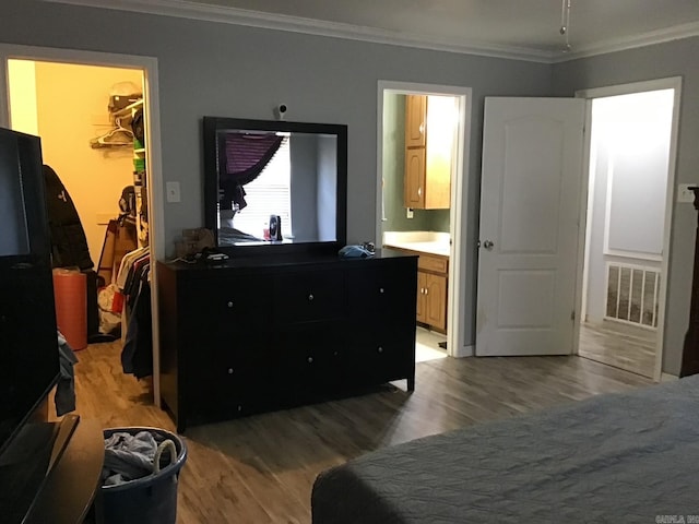 bedroom with crown molding, light hardwood / wood-style flooring, connected bathroom, a spacious closet, and a closet