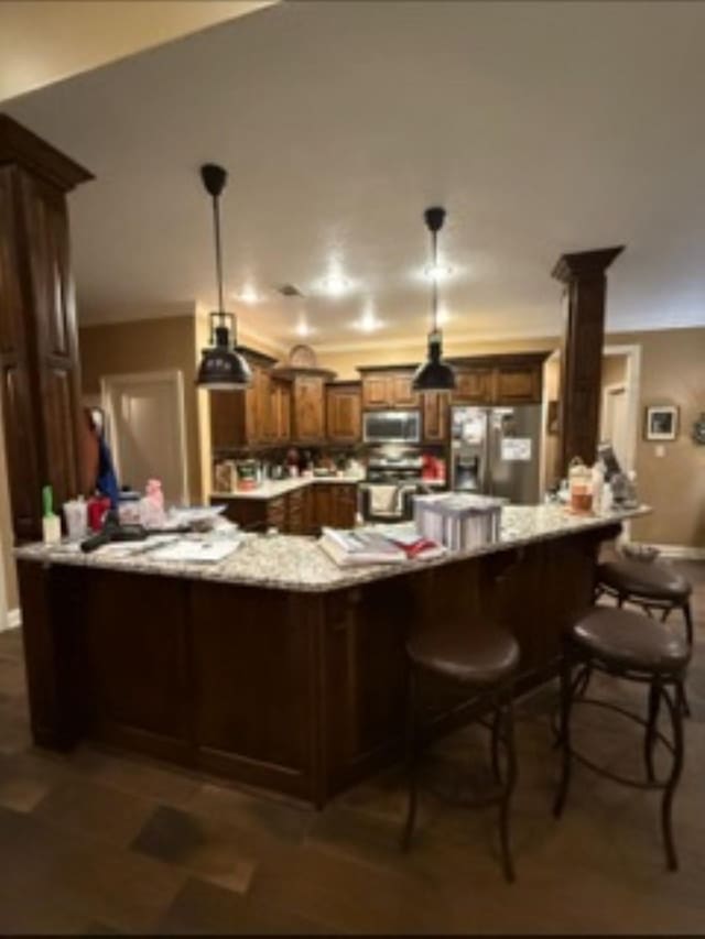 kitchen with appliances with stainless steel finishes, hanging light fixtures, a peninsula, ornate columns, and a kitchen bar