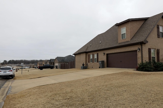 exterior space featuring brick siding, roof with shingles, concrete driveway, a garage, and cooling unit