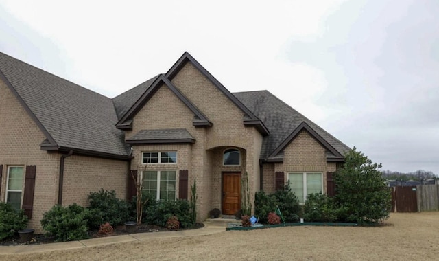 view of front of home featuring a shingled roof, a front lawn, and brick siding