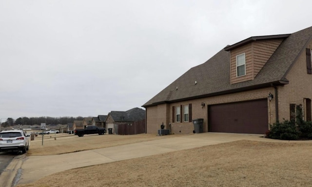 exterior space featuring central air condition unit, a garage, brick siding, a shingled roof, and concrete driveway