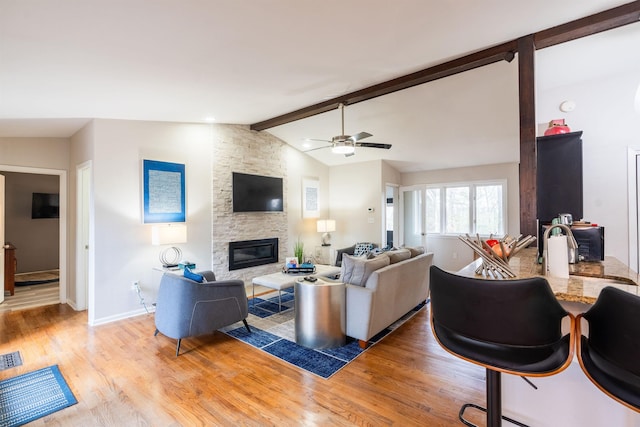 living room with lofted ceiling with beams, ceiling fan, light wood-type flooring, and a fireplace