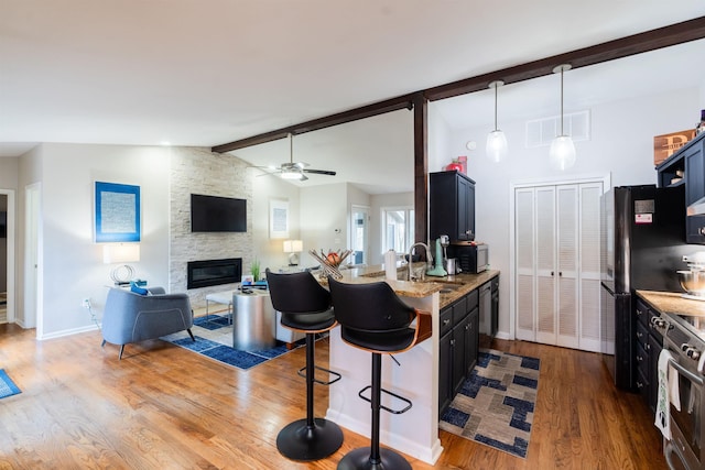 kitchen featuring a kitchen bar, sink, wood-type flooring, lofted ceiling with beams, and light stone countertops