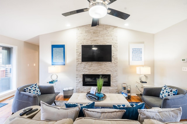 living room featuring ceiling fan, wood-type flooring, a stone fireplace, and vaulted ceiling