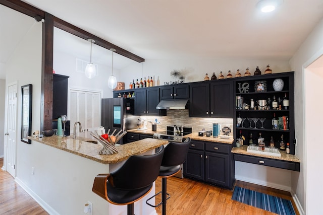 kitchen featuring stainless steel refrigerator, decorative light fixtures, lofted ceiling with beams, light stone counters, and kitchen peninsula