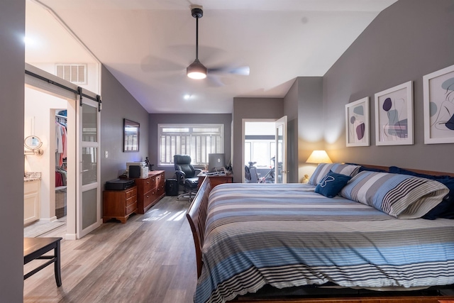 bedroom with lofted ceiling, a walk in closet, light wood-type flooring, a closet, and a barn door