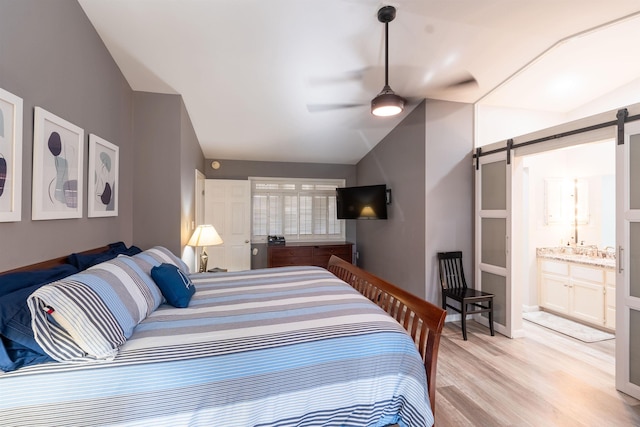 bedroom with ensuite bath, ceiling fan, vaulted ceiling, a barn door, and light wood-type flooring