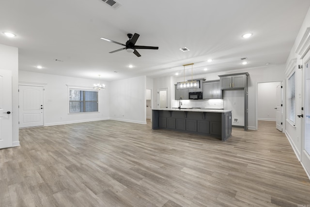 kitchen featuring pendant lighting, hardwood / wood-style flooring, gray cabinets, an island with sink, and ceiling fan with notable chandelier