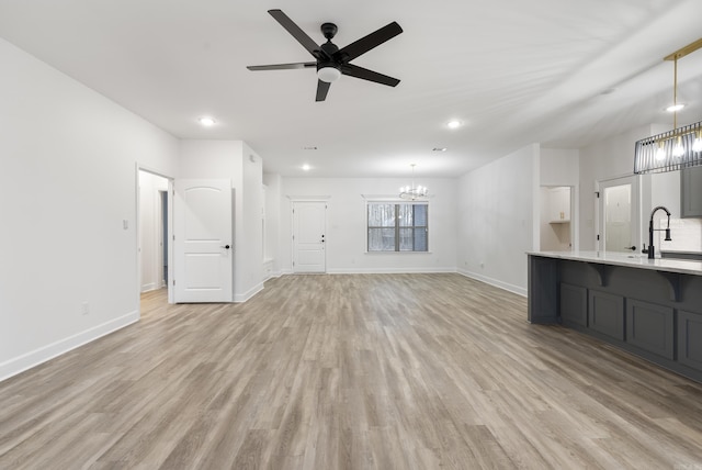 unfurnished living room featuring sink, ceiling fan with notable chandelier, and light hardwood / wood-style floors