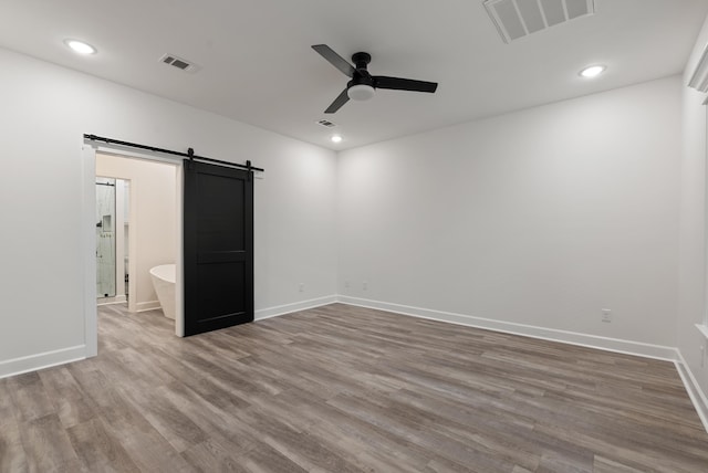 unfurnished bedroom with hardwood / wood-style flooring, a barn door, ceiling fan, and ensuite bathroom