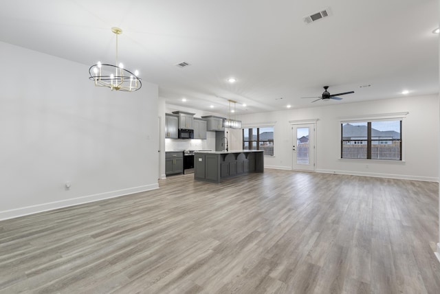 unfurnished living room with sink, ceiling fan with notable chandelier, light hardwood / wood-style floors, and a healthy amount of sunlight