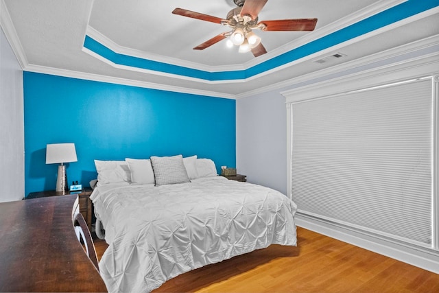 bedroom with a tray ceiling, wood-type flooring, ornamental molding, and ceiling fan