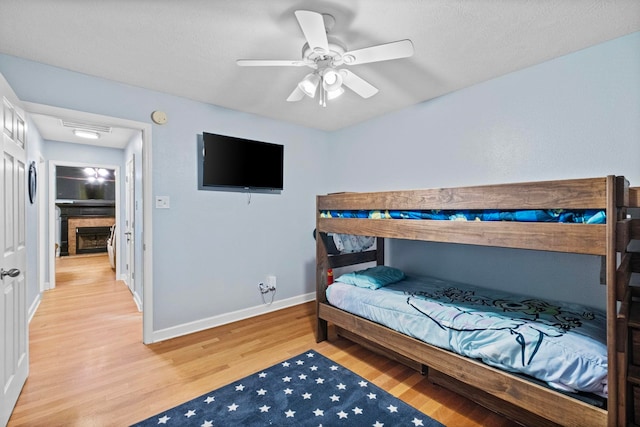 bedroom featuring a fireplace, ceiling fan, and light wood-type flooring