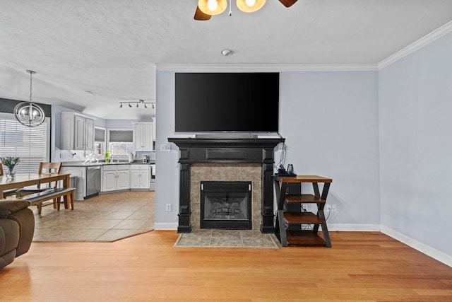 living room with a fireplace, ornamental molding, ceiling fan, a textured ceiling, and light hardwood / wood-style flooring