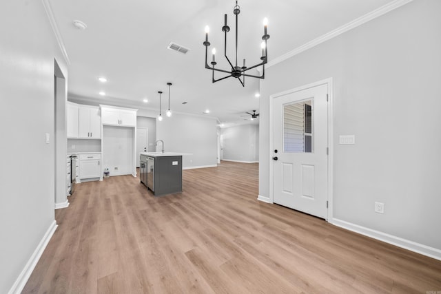 kitchen with crown molding, light hardwood / wood-style flooring, a kitchen island with sink, white cabinets, and decorative light fixtures