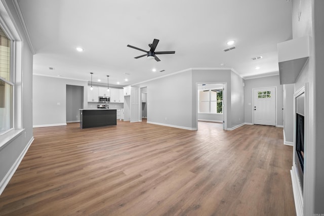 unfurnished living room featuring hardwood / wood-style floors, crown molding, and ceiling fan