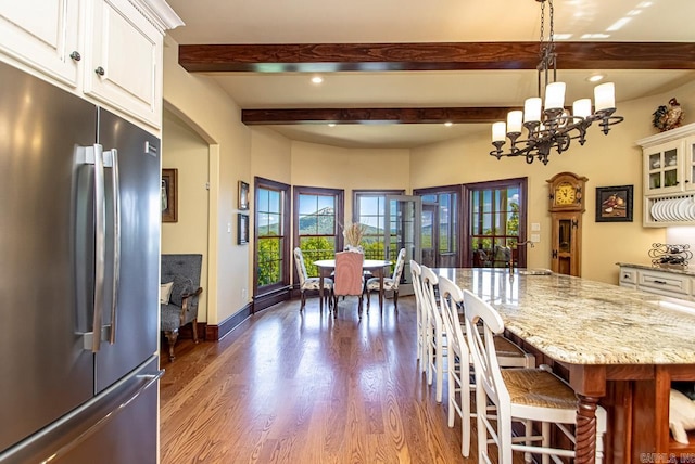 kitchen with white cabinetry, light stone counters, hanging light fixtures, stainless steel refrigerator, and dark hardwood / wood-style floors