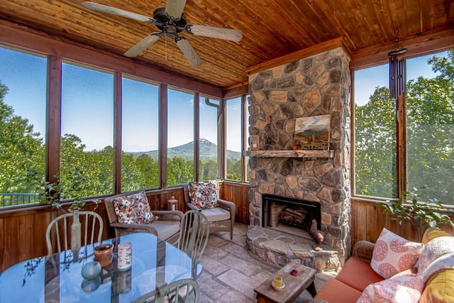 sunroom featuring ceiling fan, a mountain view, a stone fireplace, and wood ceiling