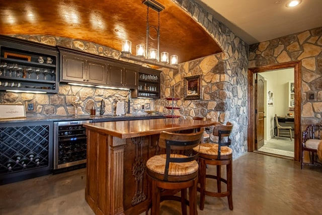 bar featuring sink, butcher block countertops, dark brown cabinets, pendant lighting, and beverage cooler