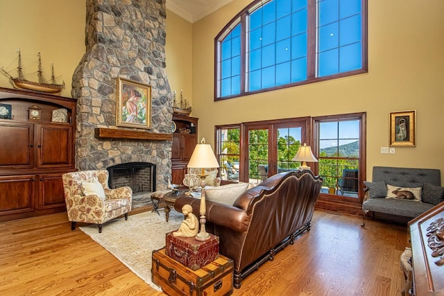 living room featuring a stone fireplace, ornamental molding, light hardwood / wood-style floors, and french doors