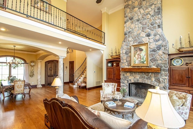 living room featuring a stone fireplace, crown molding, a chandelier, hardwood / wood-style flooring, and a high ceiling