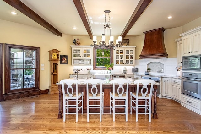 kitchen with premium range hood, stainless steel appliances, light stone countertops, a kitchen island, and decorative light fixtures