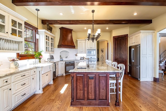 kitchen with decorative light fixtures, a center island with sink, custom range hood, and appliances with stainless steel finishes