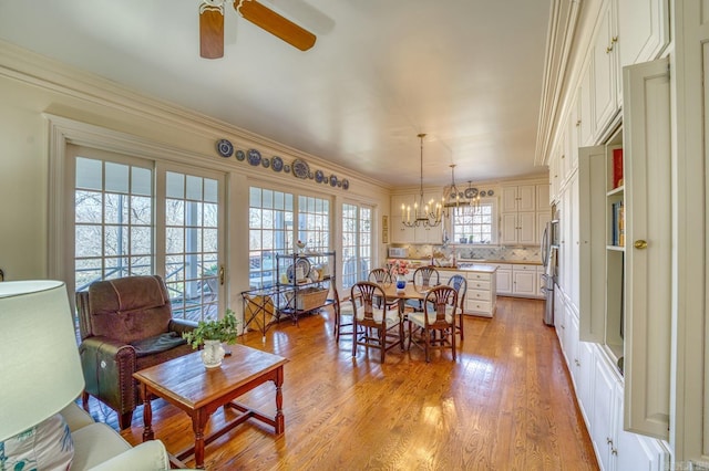 dining room featuring ornamental molding, ceiling fan with notable chandelier, and light wood-type flooring