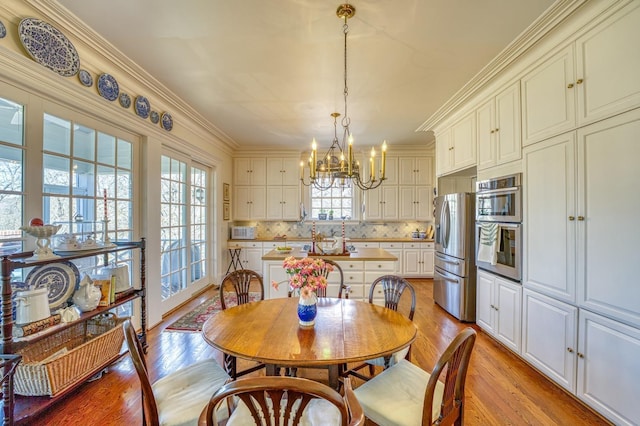 dining space with crown molding, a notable chandelier, and light hardwood / wood-style flooring