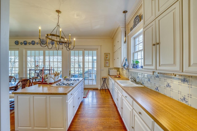 kitchen with sink, wooden counters, ornamental molding, a kitchen island, and decorative light fixtures