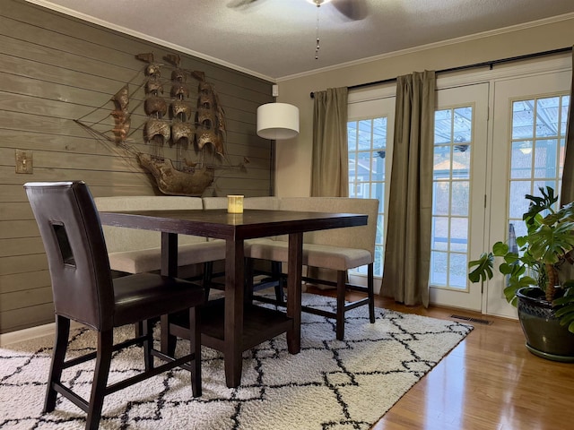 dining room with crown molding, a healthy amount of sunlight, light hardwood / wood-style floors, and wood walls