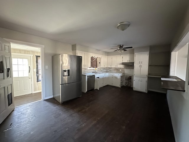 kitchen with dark wood-type flooring, ceiling fan, appliances with stainless steel finishes, white cabinetry, and tasteful backsplash