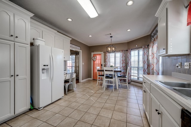 kitchen with white refrigerator with ice dispenser, white cabinets, backsplash, and decorative light fixtures