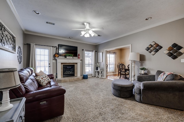 carpeted living room featuring crown molding, ceiling fan, a fireplace, and a textured ceiling