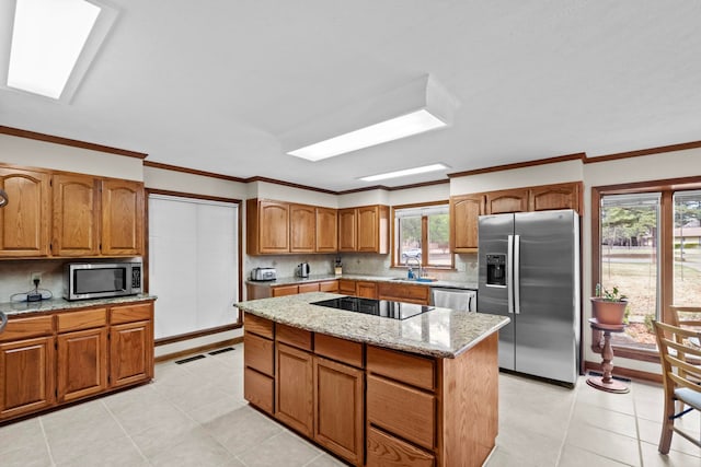 kitchen with sink, light stone counters, a center island, a skylight, and appliances with stainless steel finishes