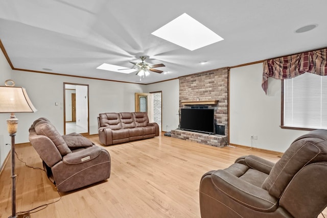 living room featuring a skylight, hardwood / wood-style flooring, ornamental molding, ceiling fan, and a brick fireplace