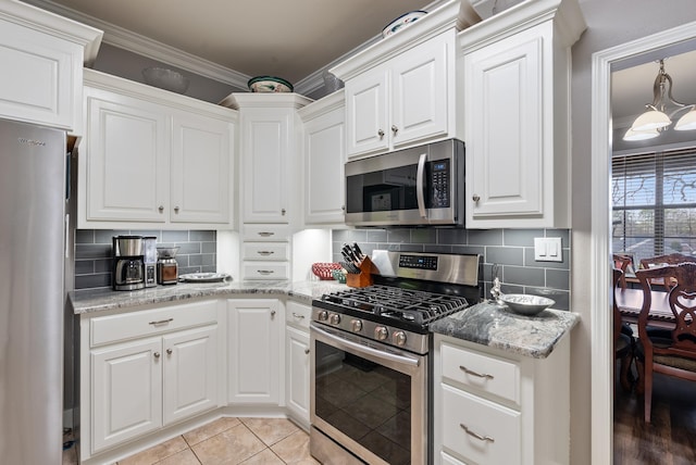 kitchen featuring light tile patterned flooring, appliances with stainless steel finishes, white cabinets, backsplash, and ornamental molding