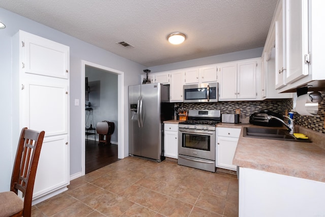 kitchen with sink, a textured ceiling, appliances with stainless steel finishes, decorative backsplash, and white cabinets