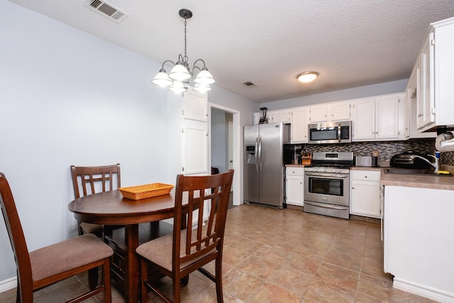 kitchen featuring pendant lighting, sink, white cabinetry, stainless steel appliances, and decorative backsplash