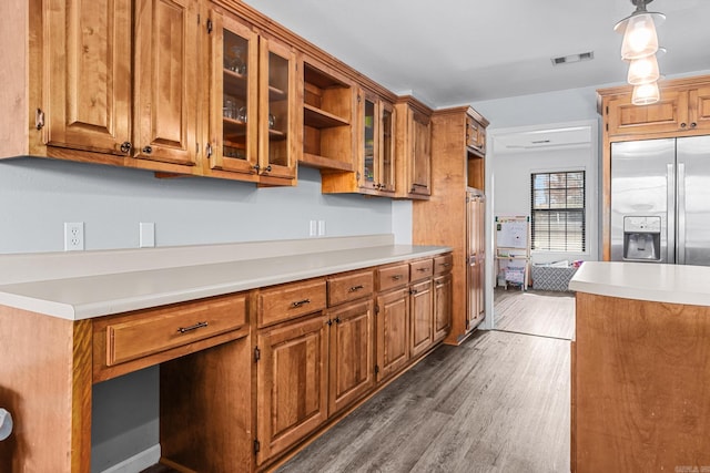 kitchen featuring visible vents, wood finished floors, stainless steel fridge, brown cabinetry, and glass insert cabinets