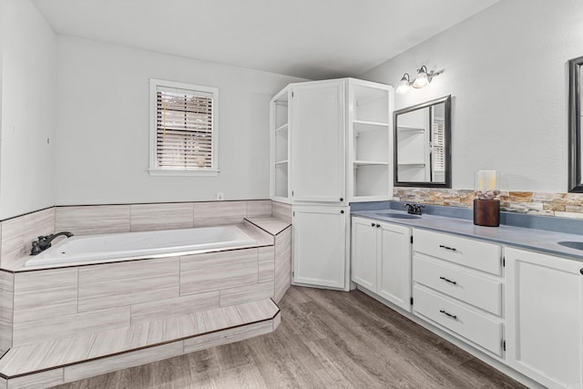 full bath with a sink, a garden tub, wood finished floors, and double vanity