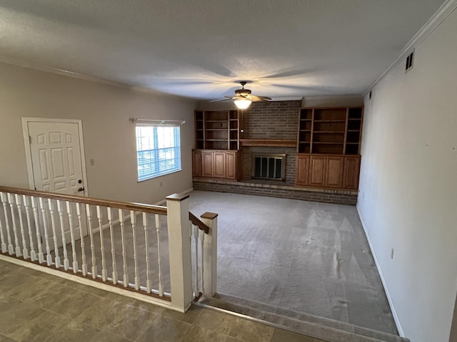 unfurnished living room featuring built in shelves, crown molding, a textured ceiling, ceiling fan, and a fireplace