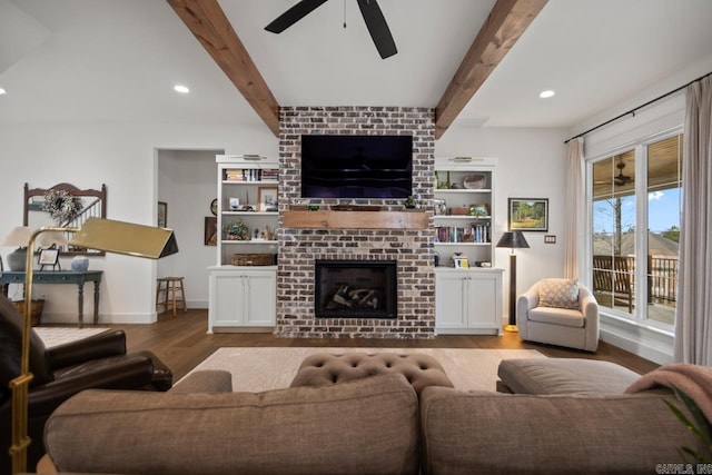 living room with ceiling fan, a brick fireplace, beam ceiling, and light hardwood / wood-style floors