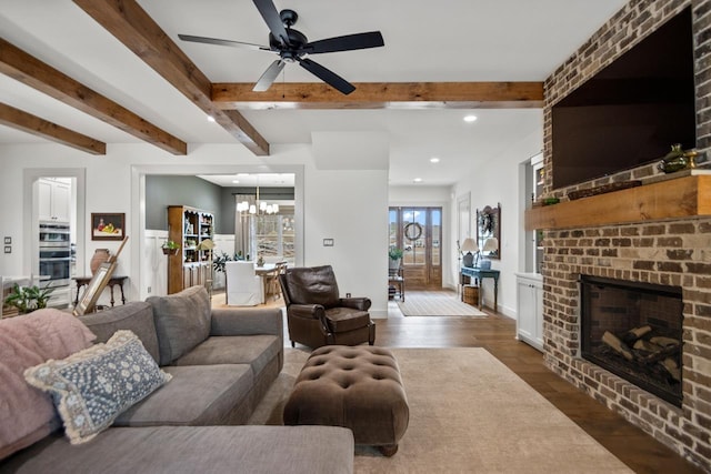 living room with beam ceiling, dark hardwood / wood-style floors, ceiling fan with notable chandelier, and a fireplace