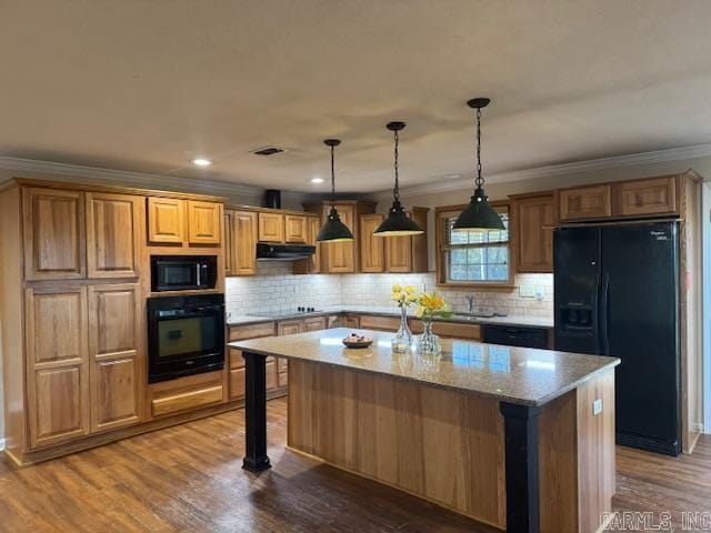 kitchen featuring dark wood-type flooring, light stone counters, ventilation hood, a center island, and black appliances