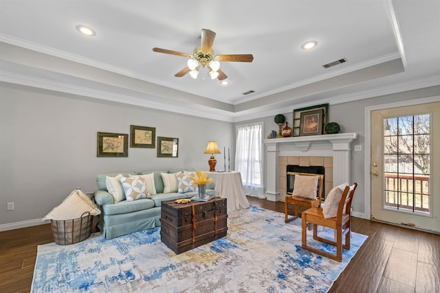 living room featuring ornamental molding, a tray ceiling, hardwood / wood-style flooring, ceiling fan, and a tiled fireplace