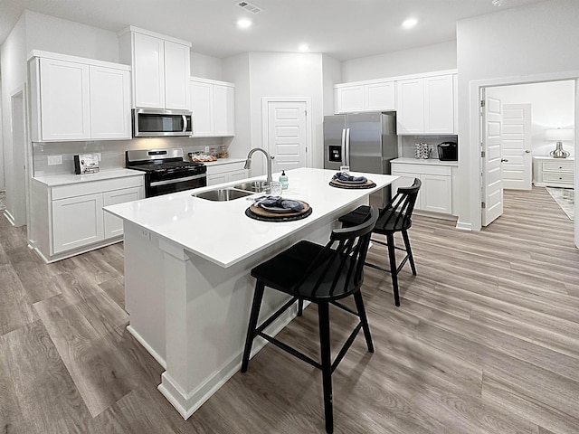 kitchen with a breakfast bar, sink, an island with sink, stainless steel appliances, and white cabinets