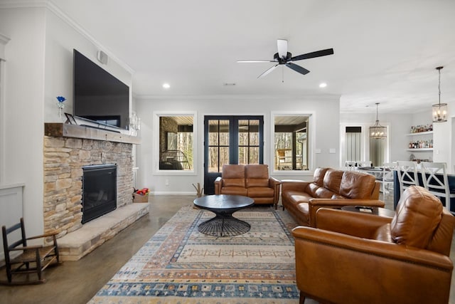 living room featuring crown molding, a stone fireplace, ceiling fan with notable chandelier, and french doors